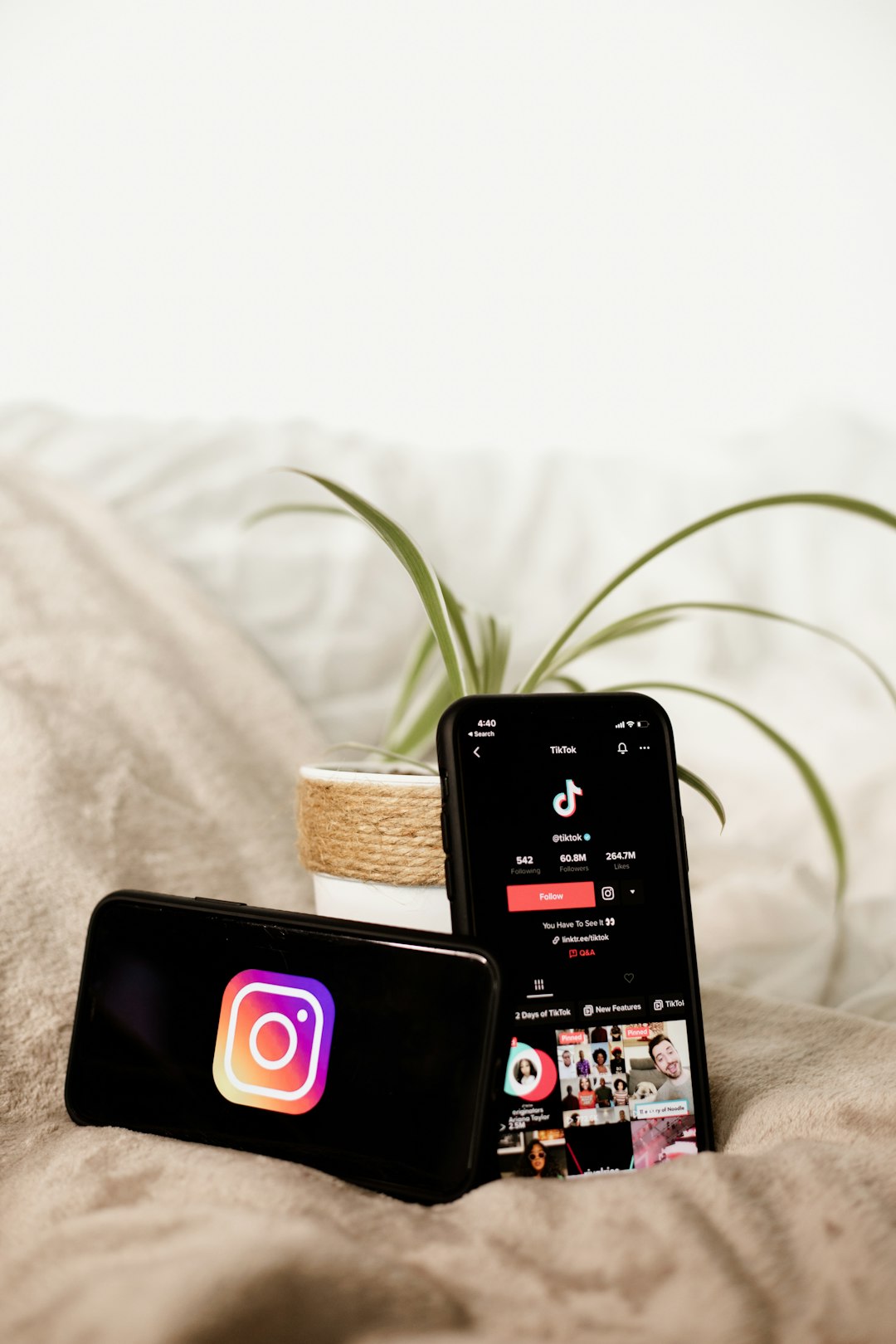 Two cell phones on a bed next to a plant